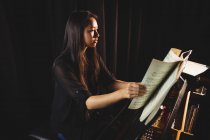 Female student looking at sheet music while playing a piano in a studio — Stock Photo