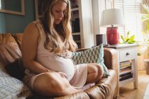 Mulher grávida relaxando na sala de estar em casa e tocando barriga — Fotografia de Stock