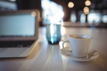 Tasse de café, verre d'eau et ordinateur portable sur la table dans le bureau — Photo de stock