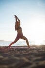 Nivel de superficie de la mujer realizando yoga en la playa en un día soleado - foto de stock