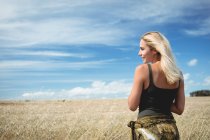 Vue arrière de la femme blonde souriante debout dans le champ — Photo de stock