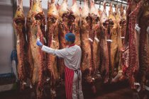Metzger klebt Etikett an rotem Fleisch, das in Abstellraum der Metzgerei hängt — Stockfoto