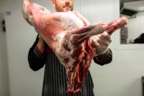 Carnicero con canal de cerdo en carnicería - foto de stock