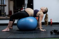 Беременная женщина выполняет упражнения на растяжку на фитнес-мяч в тренажерном зале — стоковое фото