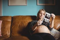 Беременная женщина смотрит на ультразвук в гостиной дома — стоковое фото
