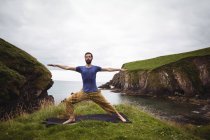 Uomo che esegue esercizio di stretching sulla scogliera — Foto stock