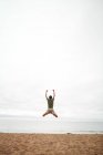 Вид сзади на человека, прыгающего на пляже — стоковое фото