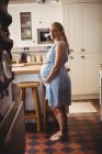 Vista lateral de Retrato de mujer embarazada de pie en la cocina en casa - foto de stock