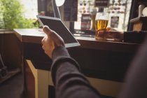 Mann benutzt digitales Tablet mit Glas Bier in der Hand an Bar — Stockfoto