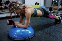 Woman doing push-up on bosu ball in gym — Stock Photo