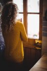 Женщина смотрит в окно, когда пьет кофе дома на кухне — стоковое фото