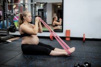 Pregnant woman exercising with resistance band in gym — Stock Photo