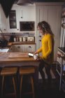 Hermosa mujer usando tableta digital mientras toma café en la cocina en casa - foto de stock