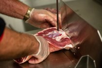 Close-up de mãos colocando um pedaço de carne na máquina de picar — Fotografia de Stock