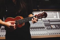 Estudante feminina de meia-seção tocando guitarra em um estúdio — Fotografia de Stock