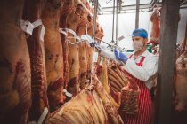 Butcher sticking barcode stickers on string in storage room at butchers shop — Stock Photo