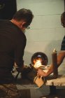 Équipe de souffleurs de verre soufflant la flamme de gaz propane sur le morceau de verre fini à l'usine de soufflage de verre — Photo de stock