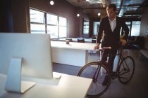 Uomo d'affari in piedi con una bicicletta in ufficio — Foto stock