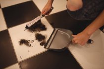 Mains du personnel féminin utilisant une poêle à poussière pour nettoyer les déchets de cheveux dans le salon — Photo de stock