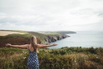 Rear view woman standing with outstretched arms on cliff over sea — Stock Photo