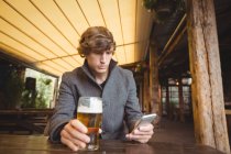 Homme utilisant un téléphone portable tout en prenant un verre de bière dans le bar — Photo de stock