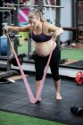 Pregnant woman exercising with resistance band in gym — Stock Photo