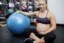 Portrait of pregnant woman holding her belly in gym — Stock Photo