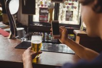 Mann mit Glas Bier mit Handy in Theke an Bar — Stockfoto