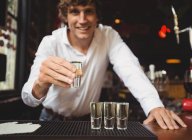 Портрет бармена, який тримає текілу, знімає скло за барною стійкою в барі — стокове фото