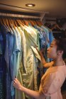 Mulher selecionando uma roupa de cabides na loja boutique — Fotografia de Stock