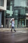 Frau hält Regenschirm und überquert Straße während Regenzeit — Stockfoto