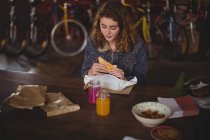 Woman sitting at table and eating sandwich in bicycle shop — Stock Photo