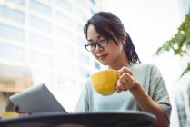 Mulher usando tablet digital enquanto toma café no café ao ar livre — Fotografia de Stock