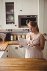 Pregnant woman reading book in kitchen at home — Stock Photo