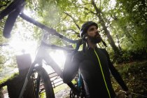 Atleta llevando una bicicleta en el bosque - foto de stock