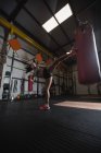 Low angle view of Female boxer practicing boxing with punching bag in fitness studio — Stock Photo