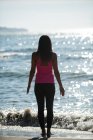 Visão traseira da mulher realizando ioga na praia no dia ensolarado — Fotografia de Stock