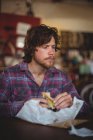 Man sitting at table and eating sandwich in bicycle shop — Stock Photo