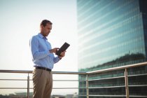 Бизнесмен с помощью цифрового планшета, стоя на балконе в офисе — стоковое фото