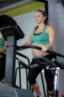 Pregnant woman exercising on elliptical machine at gym — Stock Photo