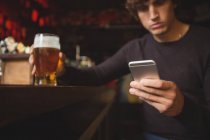 Человек, использующий мобильный телефон со стаканом пива в руке в баре — стоковое фото