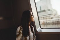Thoughtful young woman looking through window while travelling in ship — Stock Photo