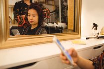 Frau benutzt Handy, während sie sich im Friseursalon die Haare glätten lässt — Stockfoto