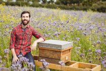 Porträt eines Imkers, der auf einem Bienenstock in einem Blumenfeld sitzt — Stockfoto