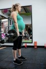Pregnant woman working out with barbell at gym — Stock Photo