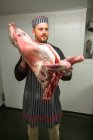Carnicero con canal de cerdo en carnicería - foto de stock