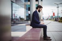 Empresário sentado na passagem do prédio de escritórios e usando laptop — Fotografia de Stock