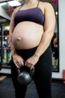 Обрезанный образ беременной женщины, поднимающей колокольчик в спортзале — стоковое фото