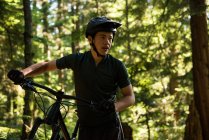 Ciclista masculino caminhando com mountain bike na floresta — Fotografia de Stock