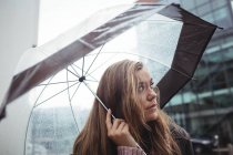 Beautiful woman holding umbrella during rainy season on street and looking up — Stock Photo